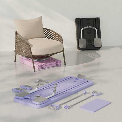 Planche de Pilates Neo Sweat violette dépliée sur le sol d'un salon avec ses accessoires prêts à l'emploi, et le modèle noir plié discrètement à côté d'un fauteuil.