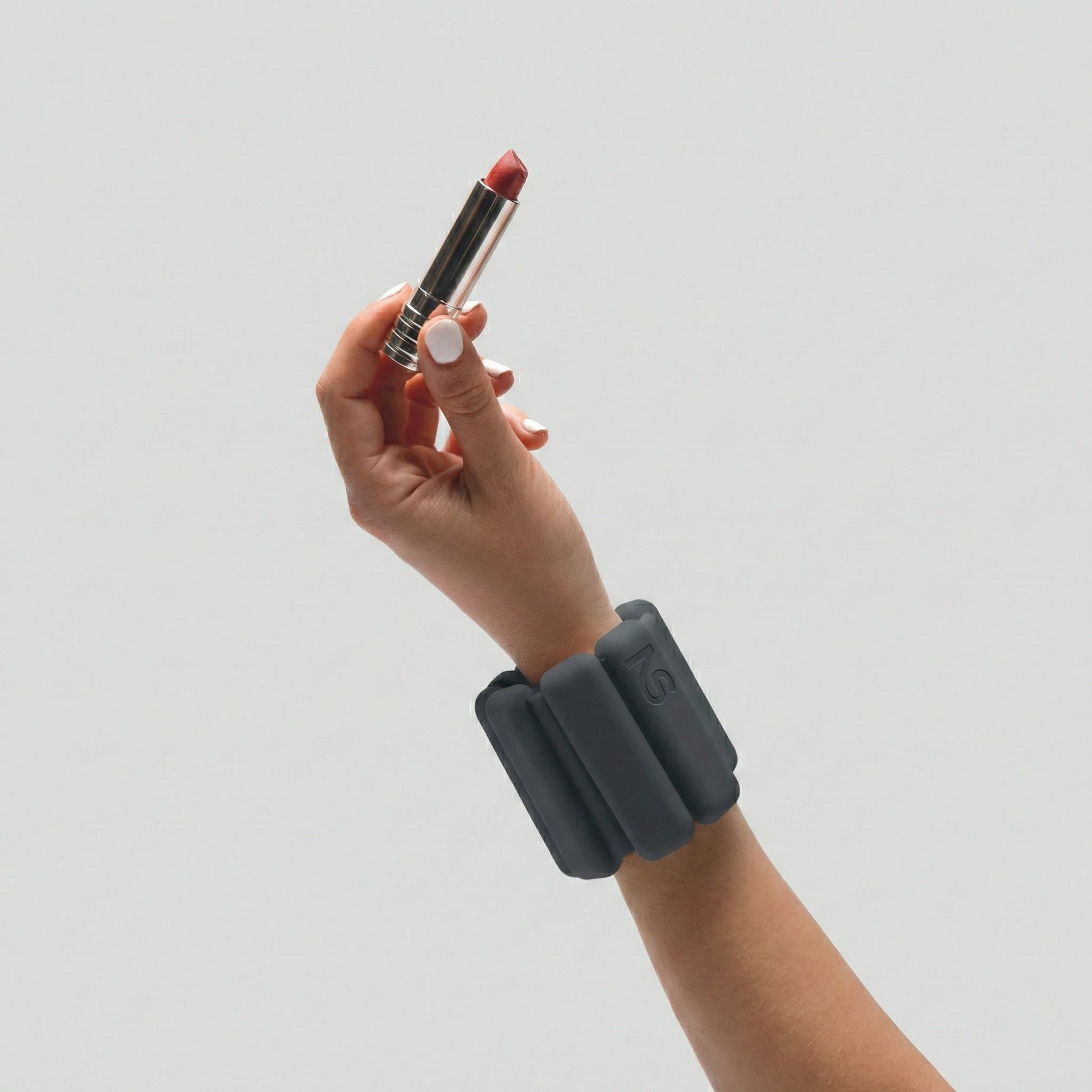 Femme portant un bracelet lesté noir Neo-Sweat au poignet en tenant un rouge à lèvres, alliant fitness à domicile et esthétisme.