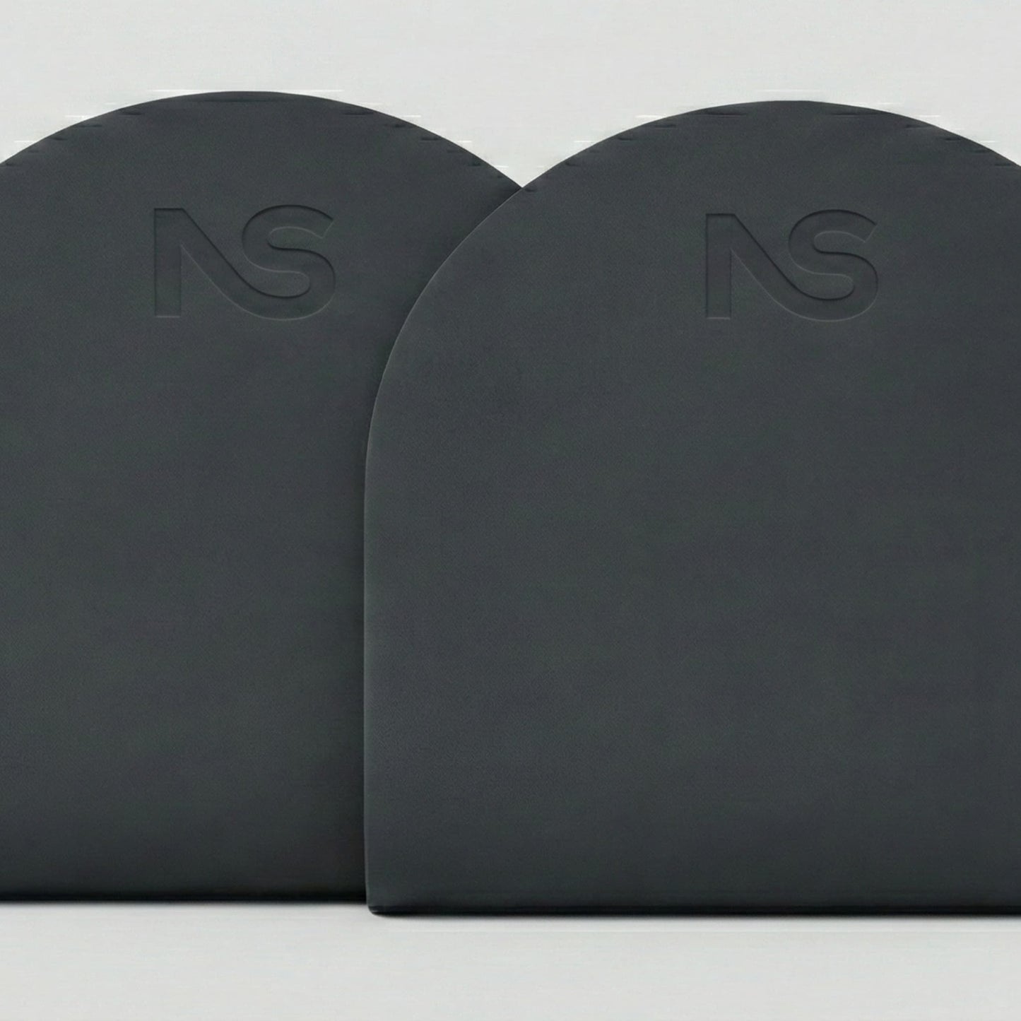 Gros plan sur les parties supérieures arrondies de deux tapis de fitness gris foncé posés côte à côte, mettant en évidence le logo subtilement gravé.