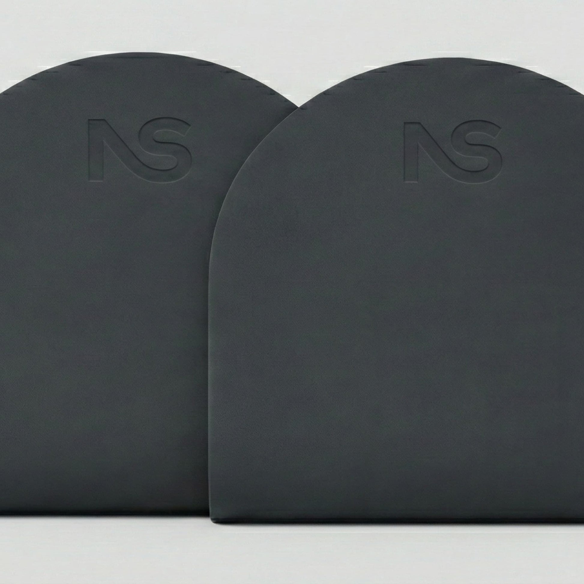 Gros plan sur les parties supérieures arrondies de deux tapis de fitness gris foncé posés côte à côte, mettant en évidence le logo subtilement gravé.