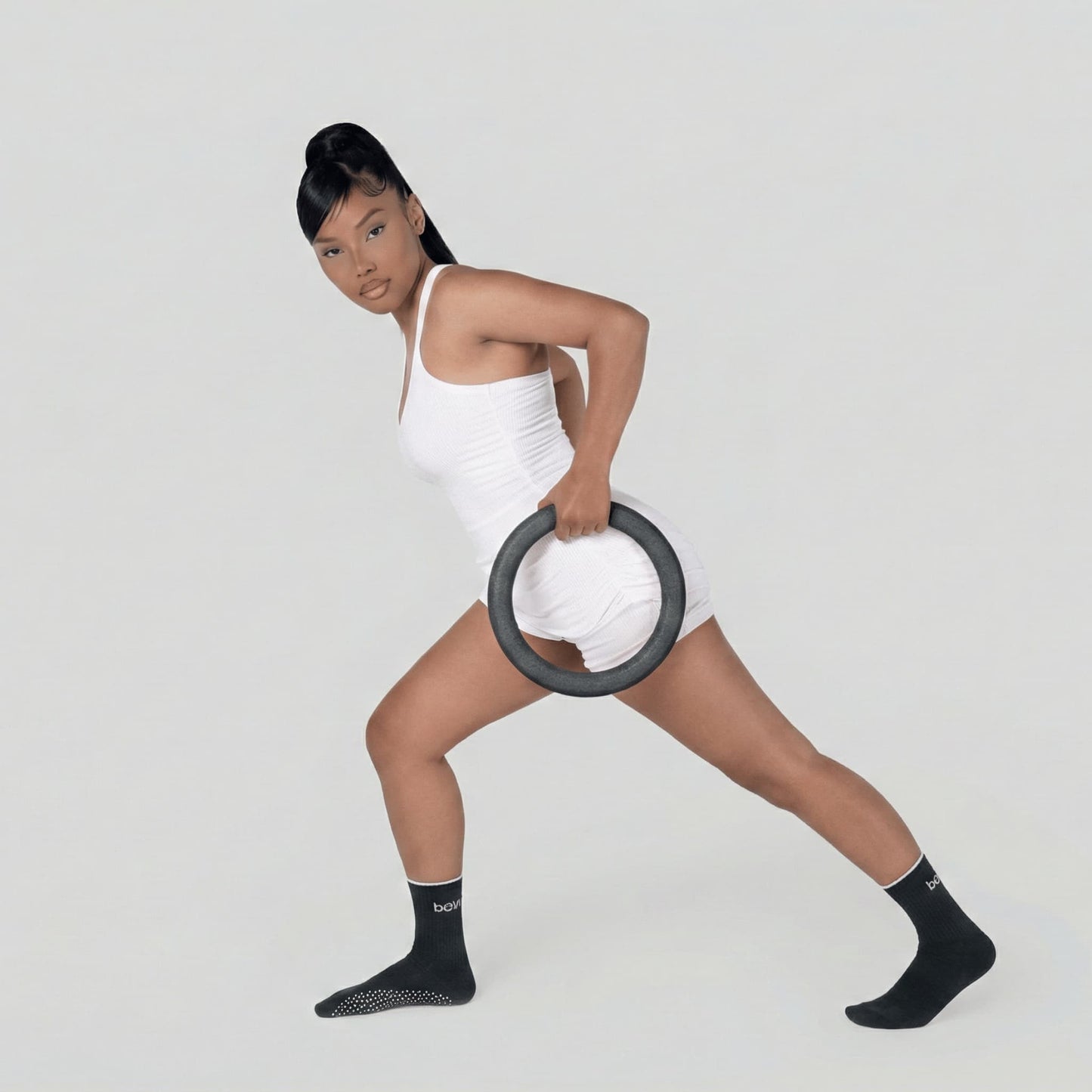 Athlète en tenue de sport blanche réalisant un exercice de fente asymétrique en tenant un anneau lesté de 4,5 kg d'une seule main.