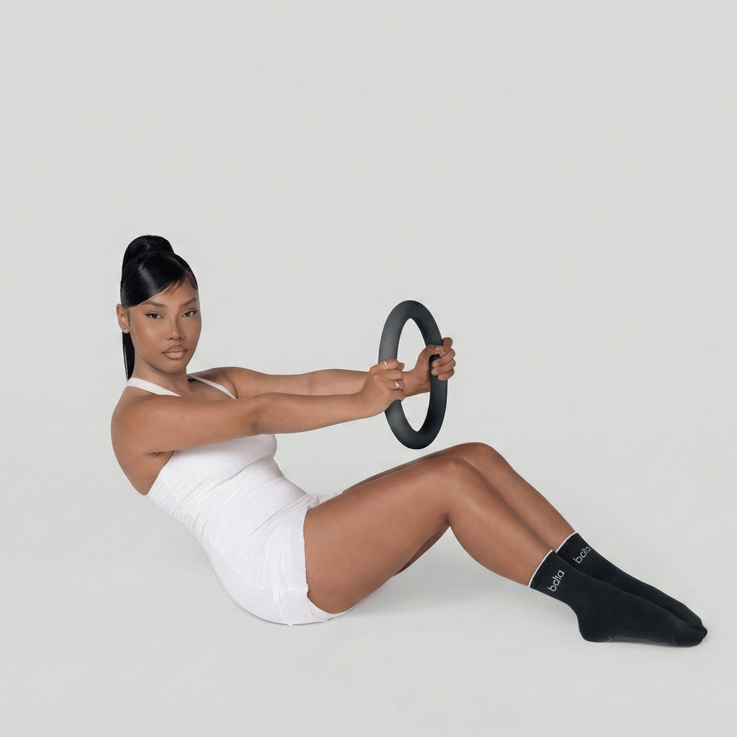 Femme en tenue de sport assise au sol, s'inclinant vers l'arrière en tenant fermement un anneau lesté de 4,5 kg devant elle pour travailler la sangle abdominale.