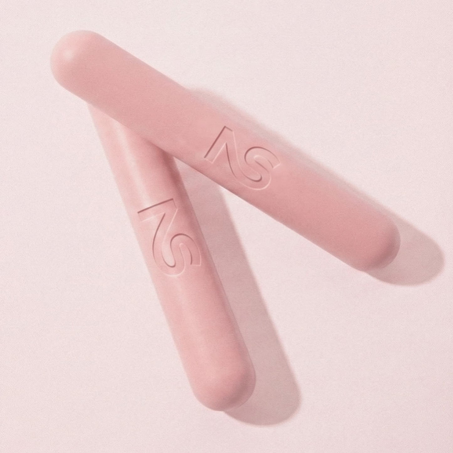 Deux haltères roses Neo Sculpt Bars croisées, soulignant leur finition mate et leur forme ergonomique innovante.