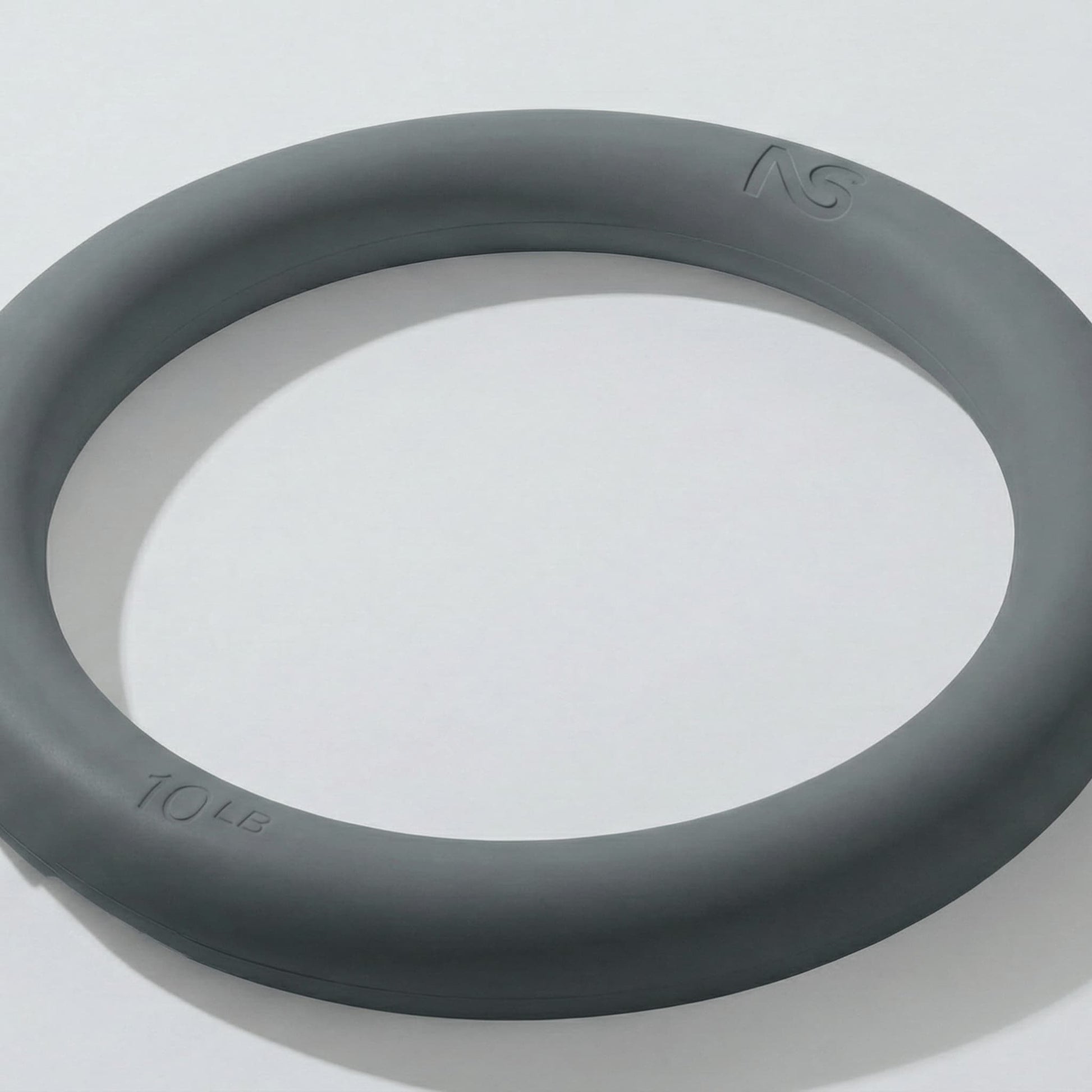 Plan rapproché incliné d'un anneau lesté gris de 4,5 kilogrammes posé sur une surface blanche, montrant ses bords arrondis et ergonomiques.
