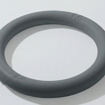 Plan rapproché incliné d'un anneau lesté gris de 4,5 kilogrammes posé sur une surface blanche, montrant ses bords arrondis et ergonomiques.
