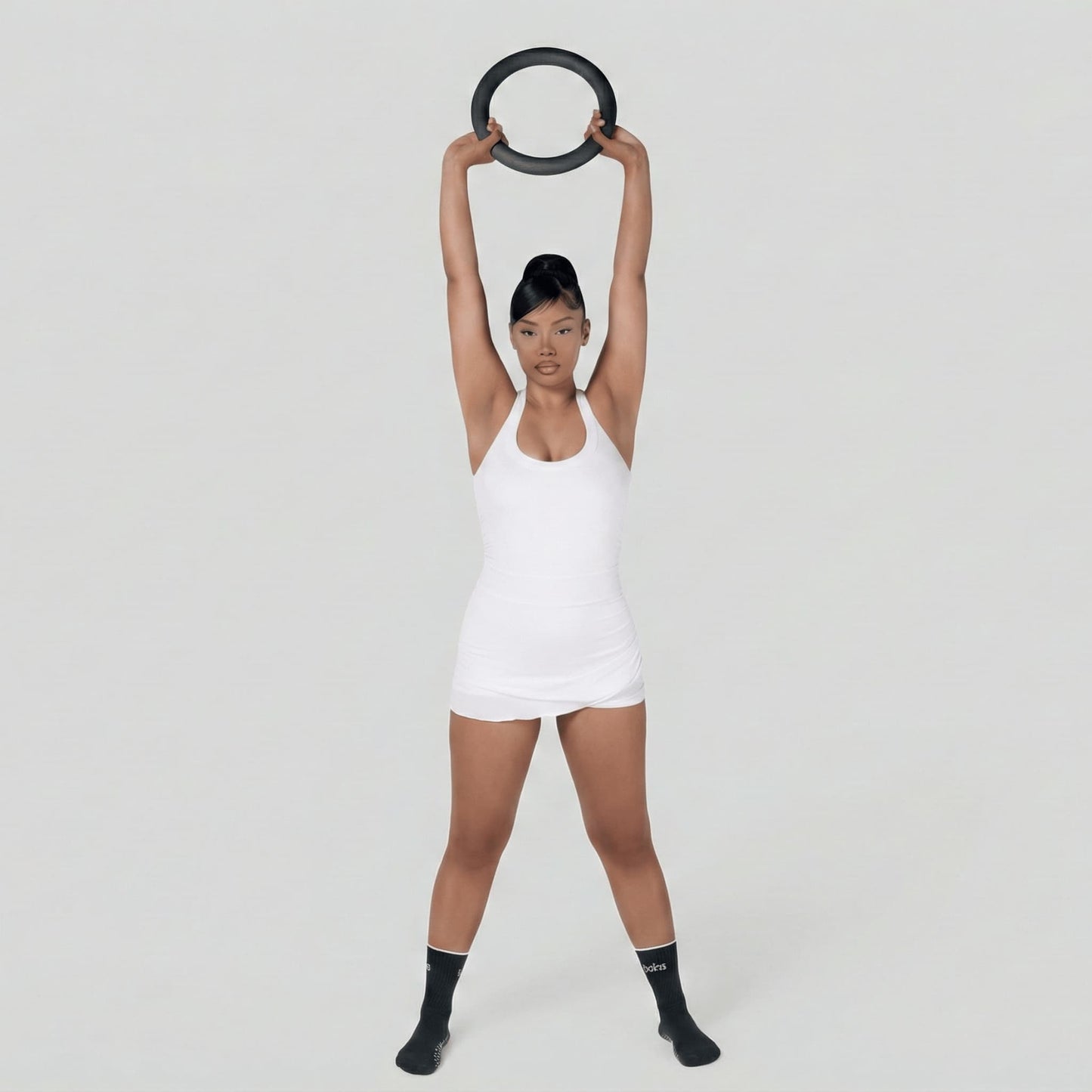 Femme en tenue de fitness blanche debout, soulevant un poids en forme de cercle de 4,5 kg à deux mains au-dessus de sa tête