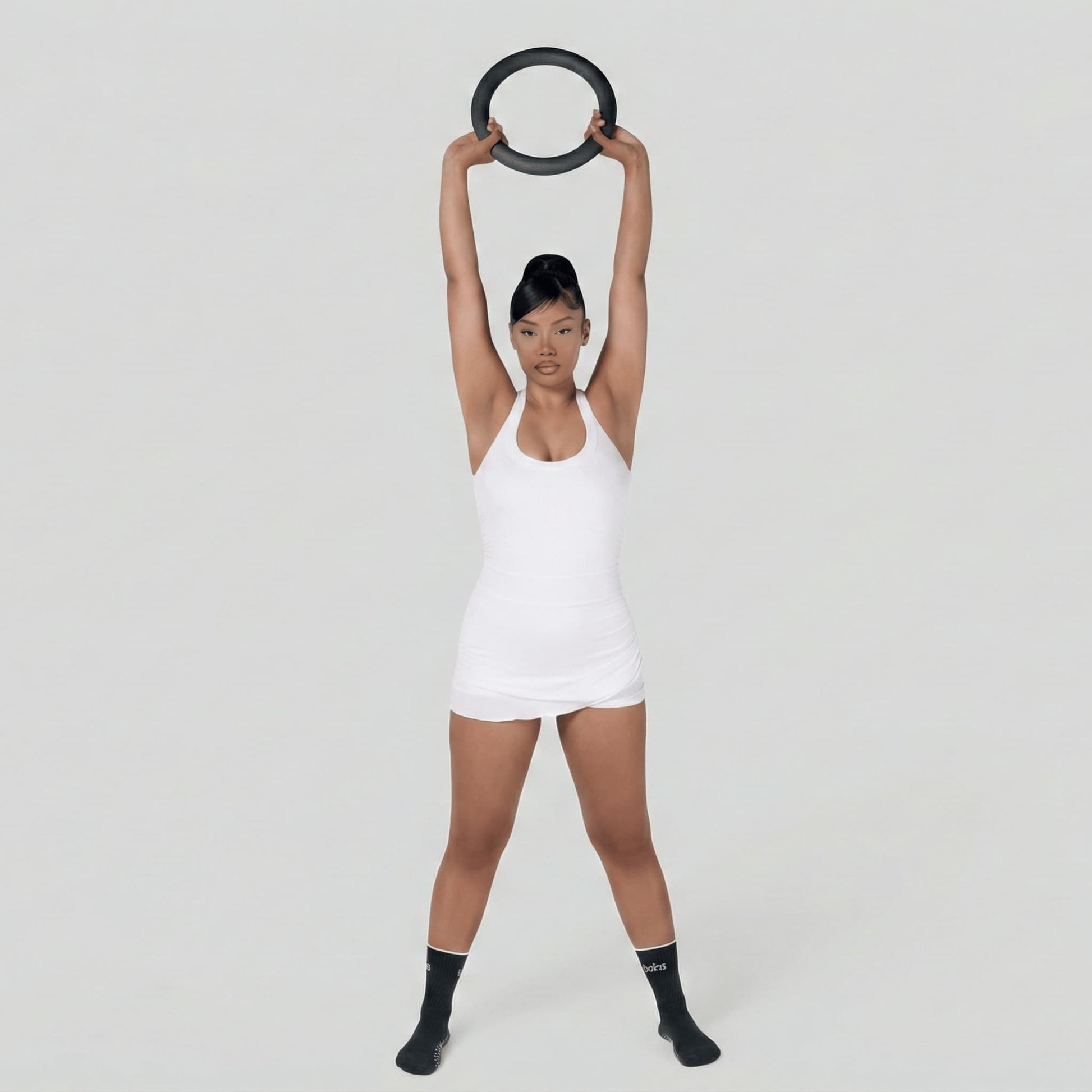 Femme en tenue de fitness blanche debout, soulevant un poids en forme de cercle de 4,5 kg à deux mains au-dessus de sa tête