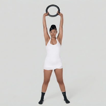 Femme en tenue de fitness blanche debout, soulevant un poids en forme de cercle de 4,5 kg à deux mains au-dessus de sa tête